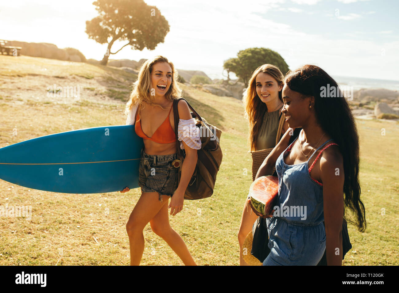 Trois femmes gaies sur une maison de marcher dans un parc à se parler. Smiling woman walking près de la mer avec des amis portant un surf. Banque D'Images