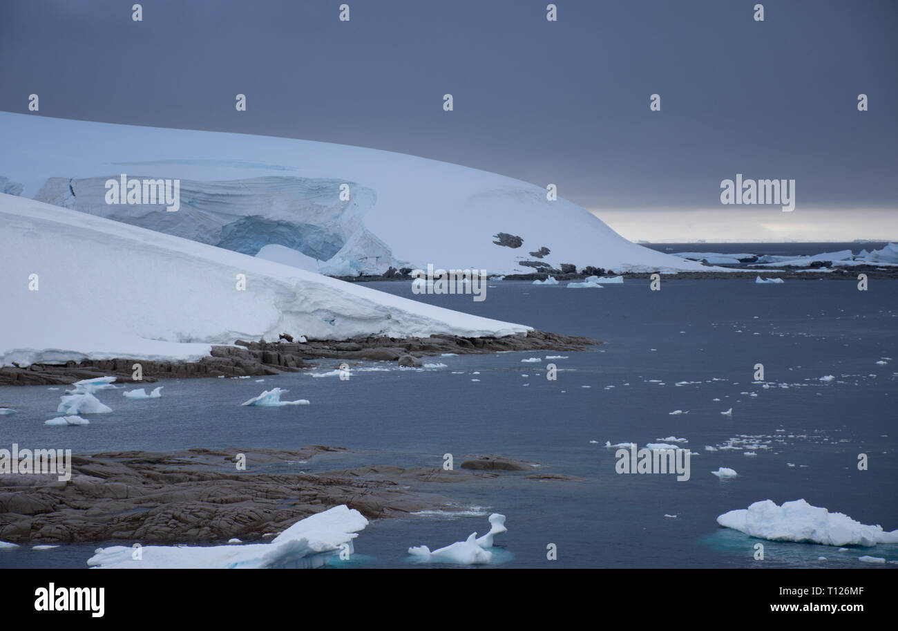 Charlotte Bay au point du portail dans l'Antarctique en vertu de cloudly skies. Le littoral est rocheux exposés et un immense glacier est dans l'arrière-plan. Banque D'Images