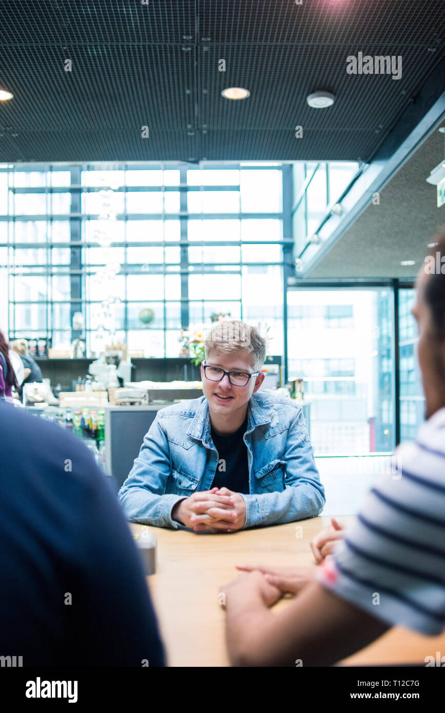 Un groupe de jeunes gens assis autour d'une table à discuter avec l'autre. Banque D'Images