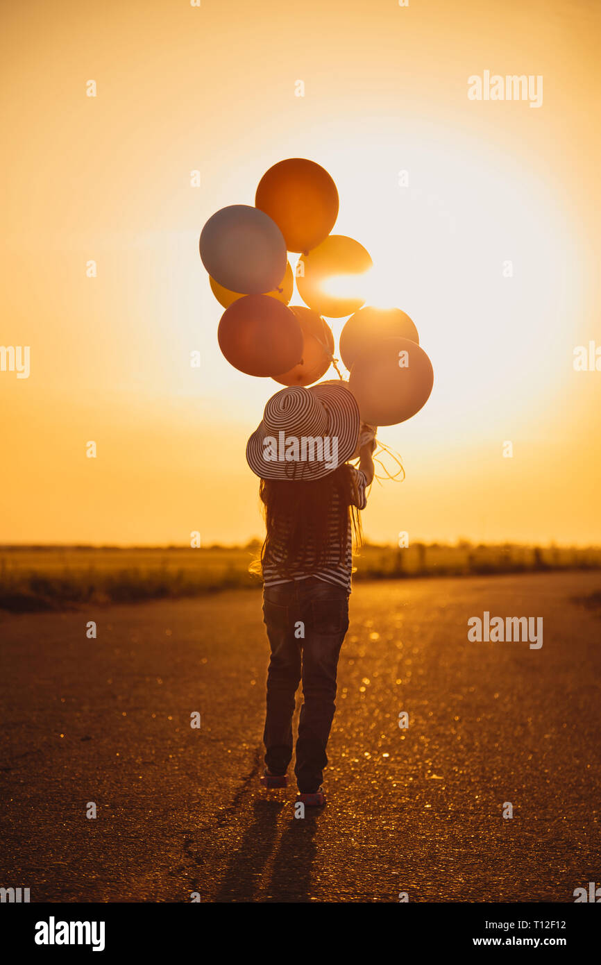 Petite fille qui marche avec des ballons colorés sur la route dans la zone au coucher du soleil. La liberté d'été et les voyages. Espérons que concept. Les émotions et sentiments. Banque D'Images