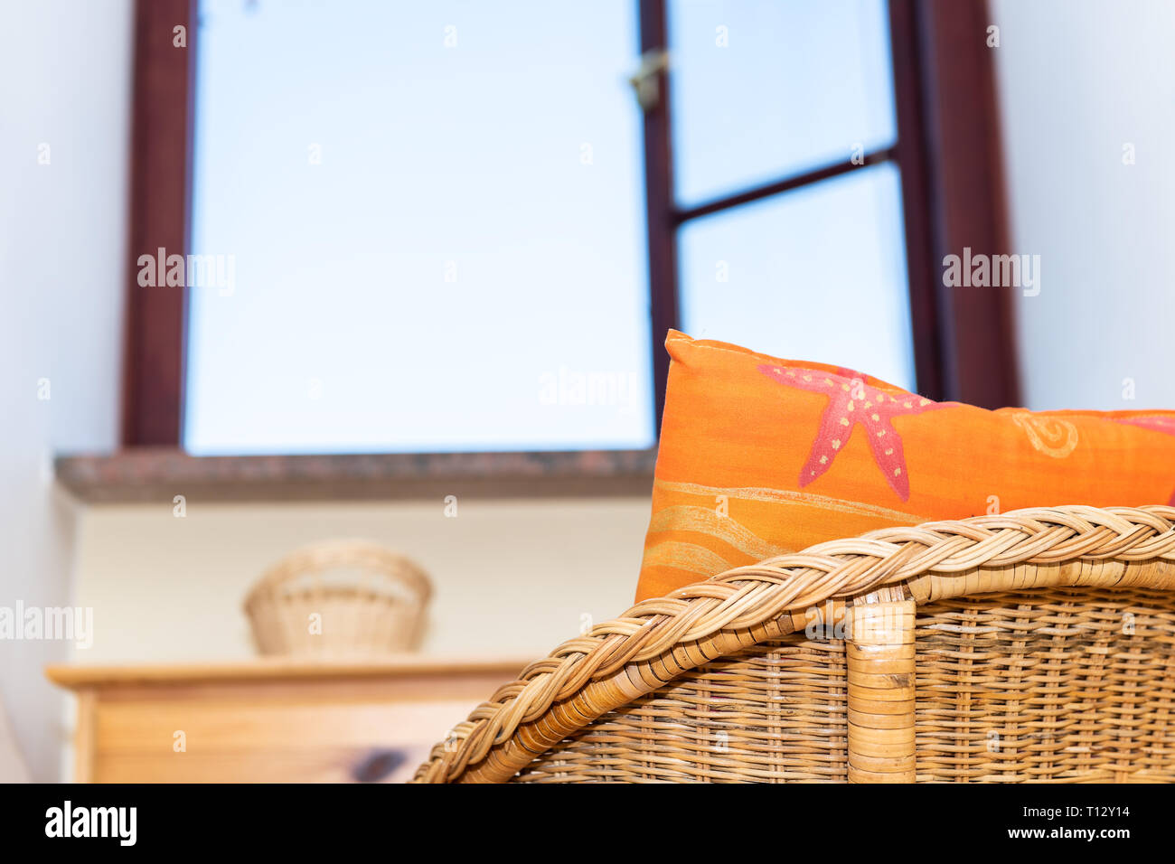 Un confortable fauteuil de paille vintage home ou maison de séjour ou chambre par la fenêtre ouverte et le ciel avec oreiller orange plage closeup Banque D'Images