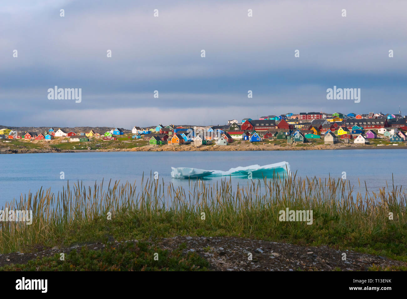 Iceberg flottant, plage noire et maisons aux couleurs vives, Qeqertarsuaq, Groenland Banque D'Images
