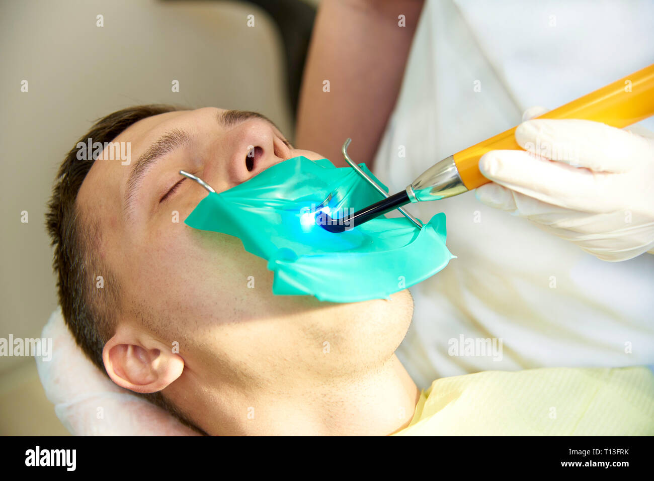 Un jeune homme aux yeux clos sur le fauteuil dentaire. Le dentiste travaille avec une lampe de polymérisation dentaire. Banque D'Images