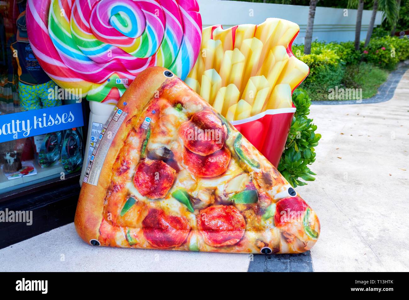 Fast food lumineux et colorés jouets gonflables y compris des pizzas, des frites ou des chips et d'une sucette à l'extérieur d'une boutique de souvenirs dans une jolie plage caribbe Banque D'Images