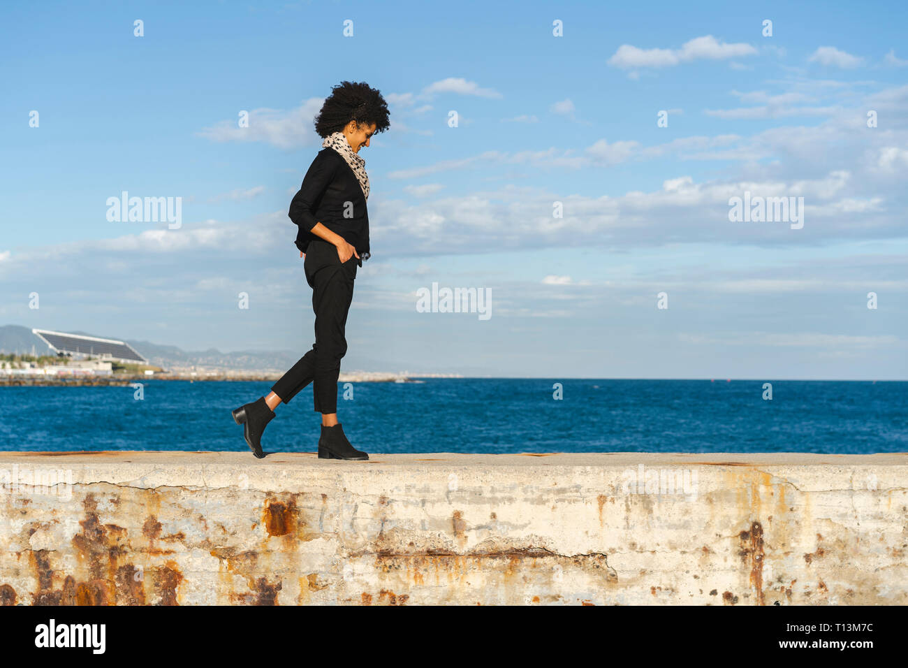 Espagne, Barcelone, laughing woman dressed in black marche sur mur à la lumière du soleil Banque D'Images