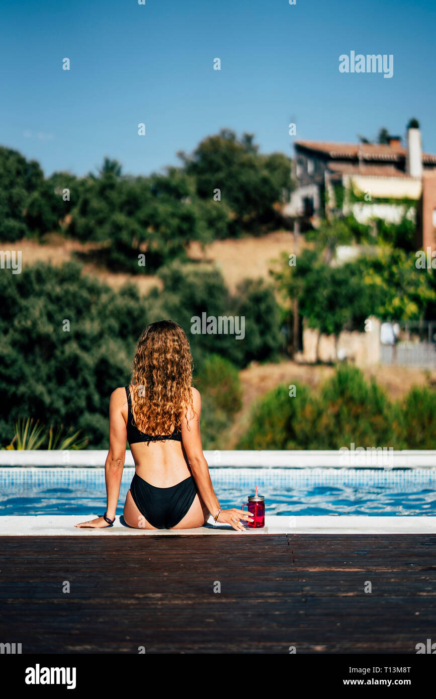 Jolie femme dans un maillot de bain de soleil au bord de la piscine, vue arrière Banque D'Images