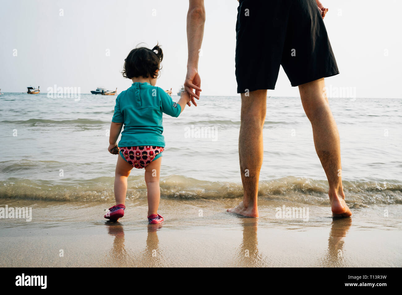 La Thaïlande, Koh Lanta, vue arrière de baby girl wearing UV protection shirt debout avec son père à bord de mer Banque D'Images