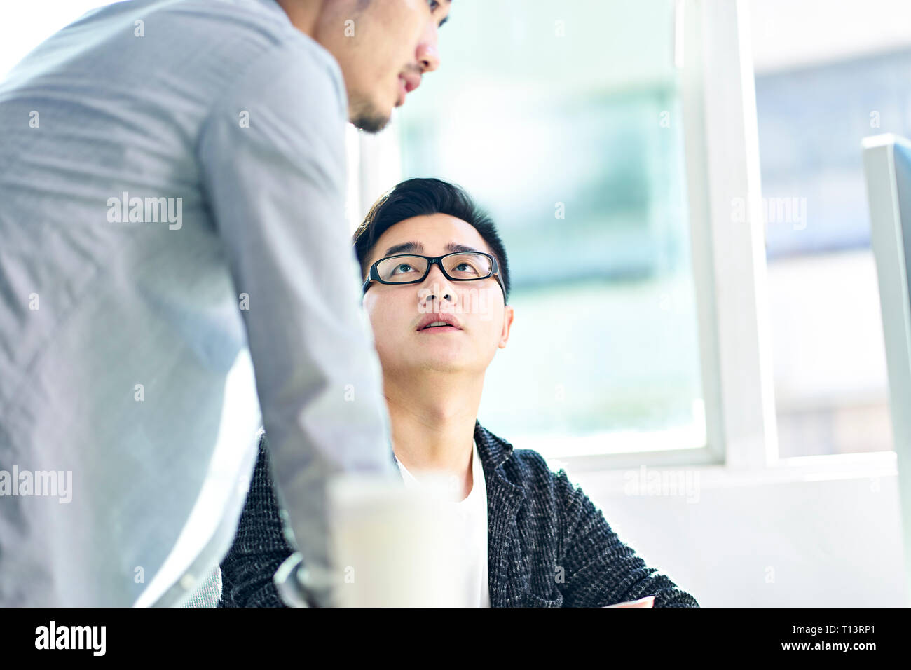 Deux jeunes hommes d'Asie ayant une discussion en avant de l'ordinateur dans le bureau. Banque D'Images