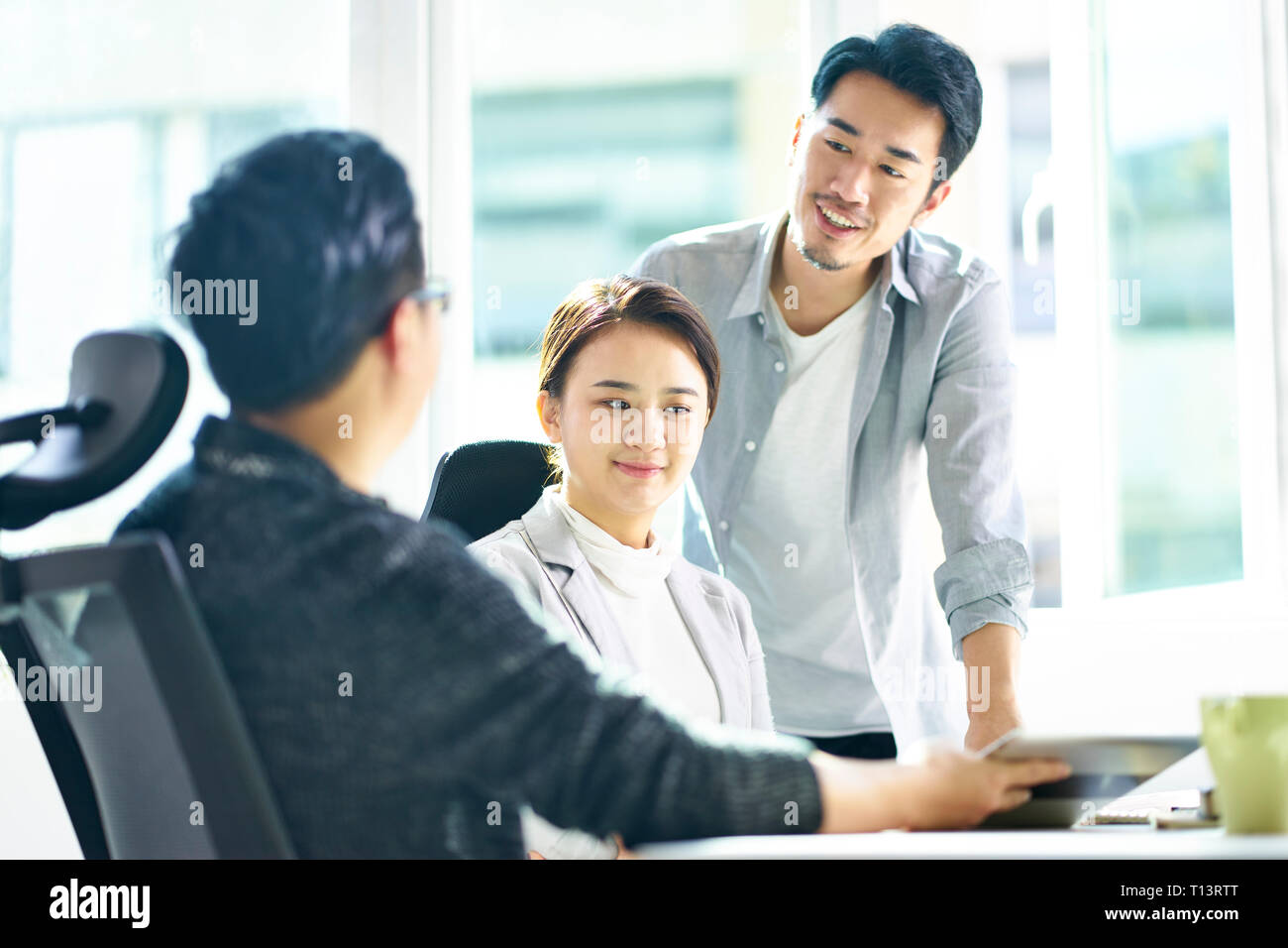 Trois jeunes dirigeants de sociétés asiatiques meeting in office discuter affaires using digital tablet. Banque D'Images