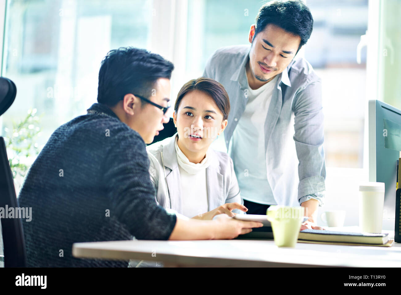 Trois jeunes dirigeants de sociétés asiatiques meeting in office discuter affaires using digital tablet. Banque D'Images