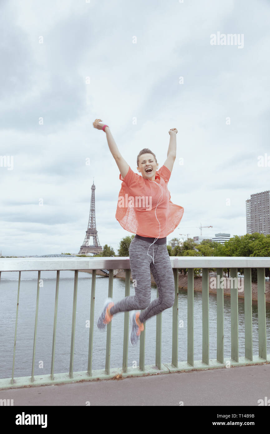 Smiling fit woman jogger en vêtements de sport à l'avant de la tour Eiffel à Paris, France le saut. Banque D'Images