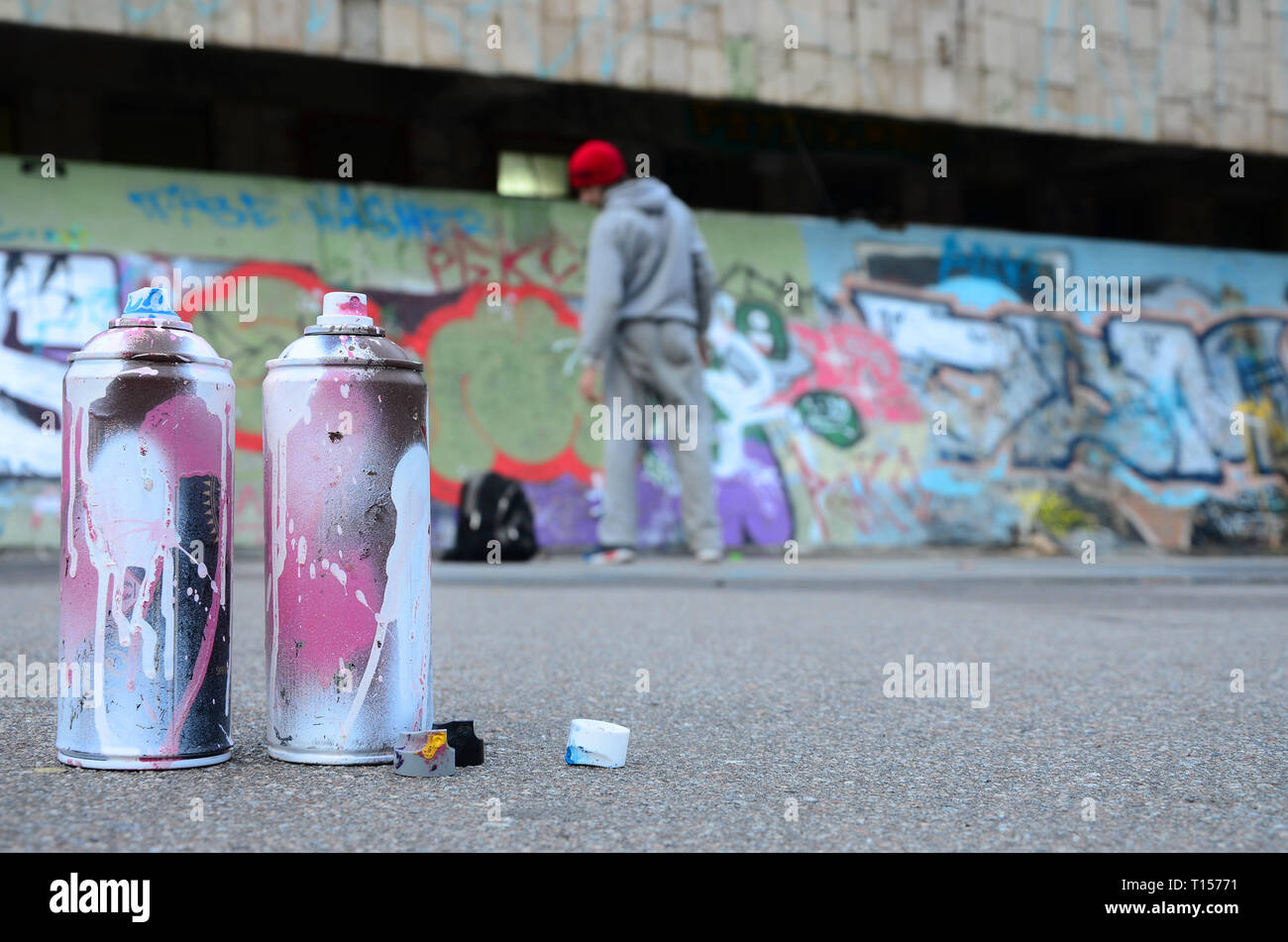 Plusieurs bombes aérosols utilisés avec la peinture blanche et rose se trouvent sur l'asphalte contre le comité permanent guy devant un mur peint de couleur en dessins graffiti Banque D'Images