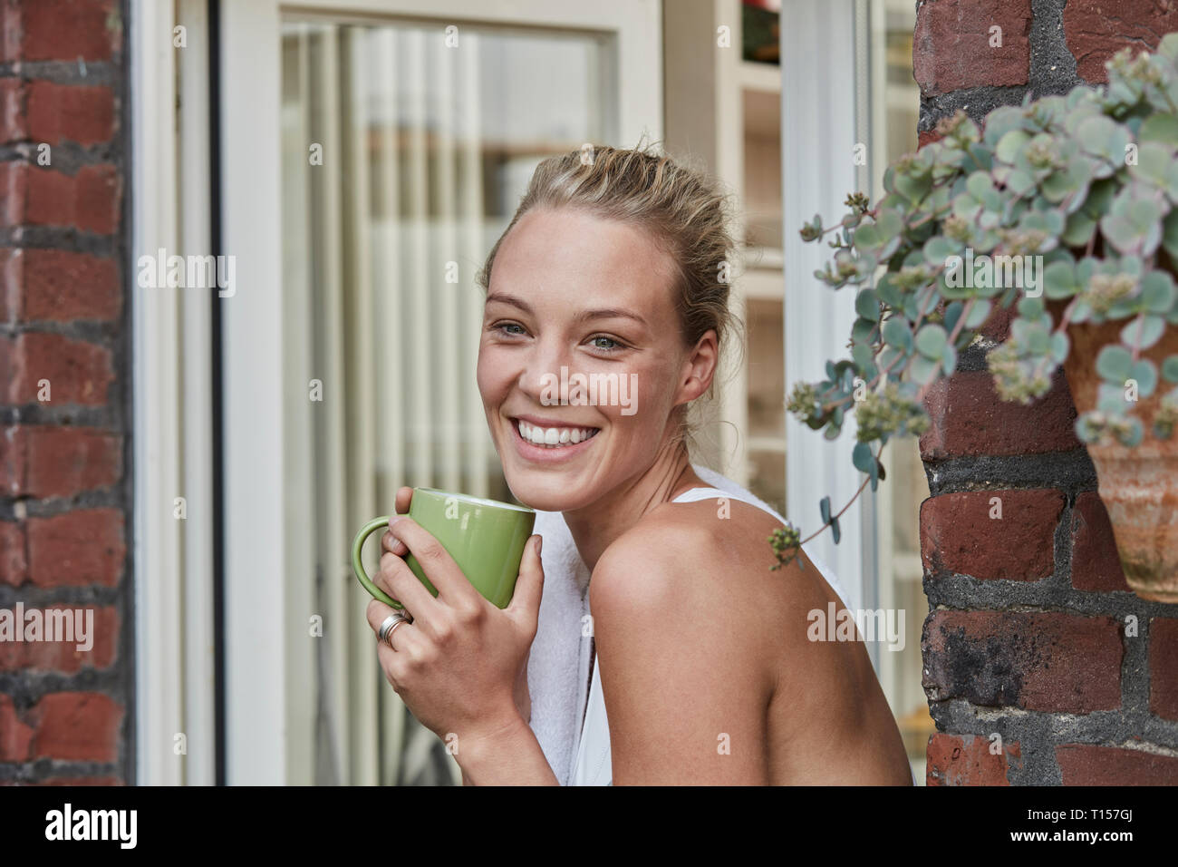 Portrait of smiling young woman sportive avec une tasse de café à l'entrée de la maison Banque D'Images