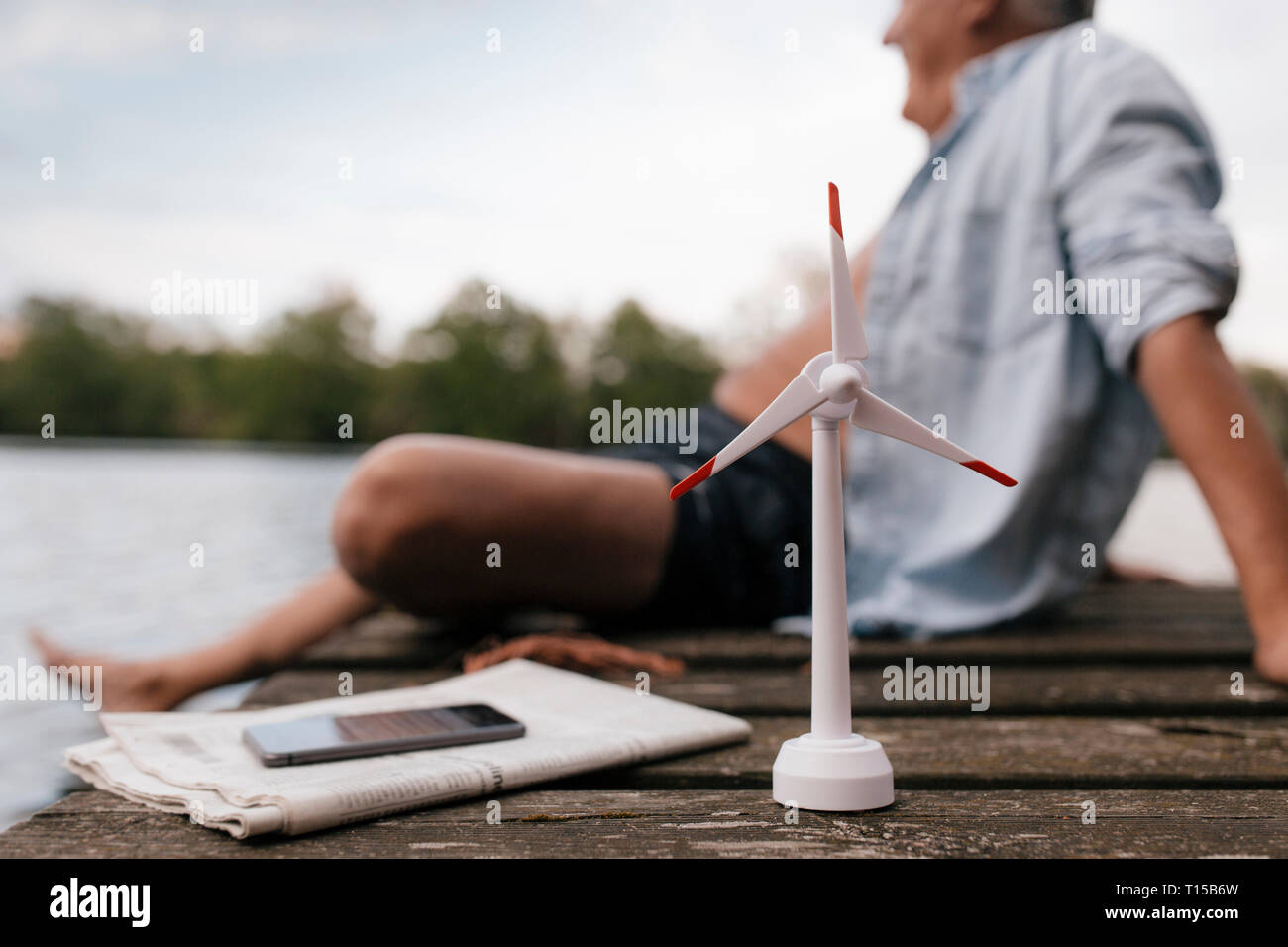 Senior man sitting on jetty à un lac avec petit modèle d'éolienne Banque D'Images