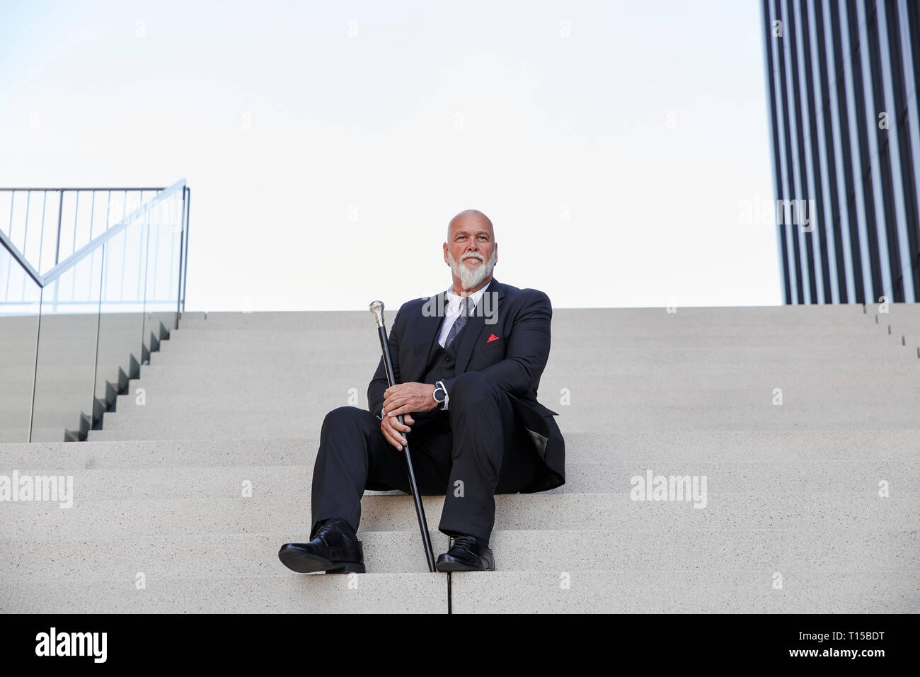 Elegant businessman avec canne, assis sur les escaliers dans la ville Banque D'Images