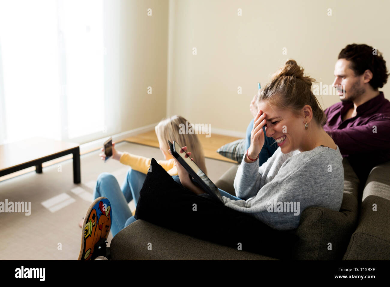 Friends sitting on couch in living, à l'aide d'appareils numériques Banque D'Images