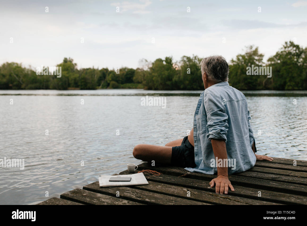 Senior man sitting on jetty at a lake Banque D'Images