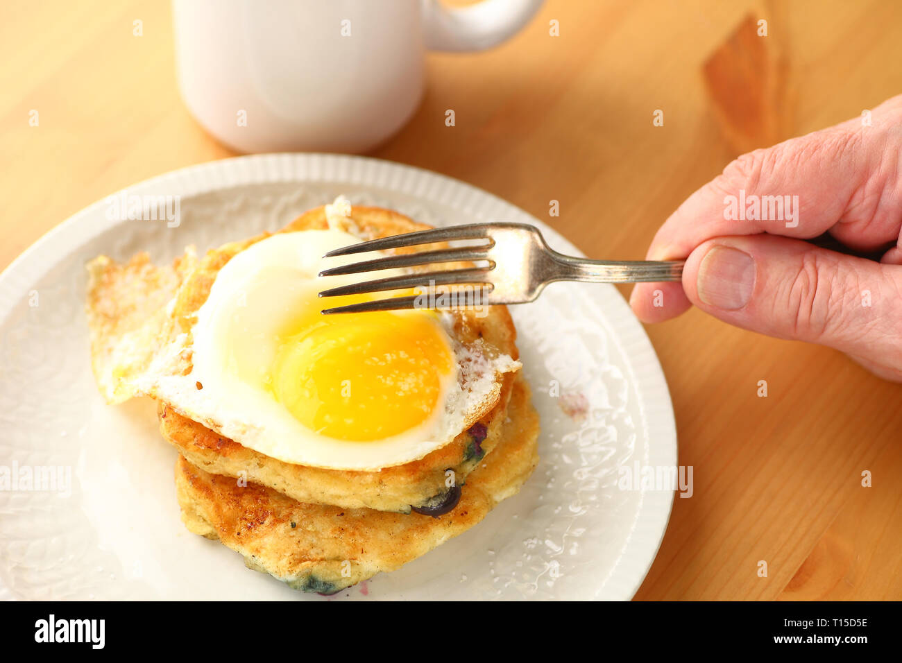 Pancakes aux myrtilles surmontée d'œuf frit avec man's hand holding fork Banque D'Images