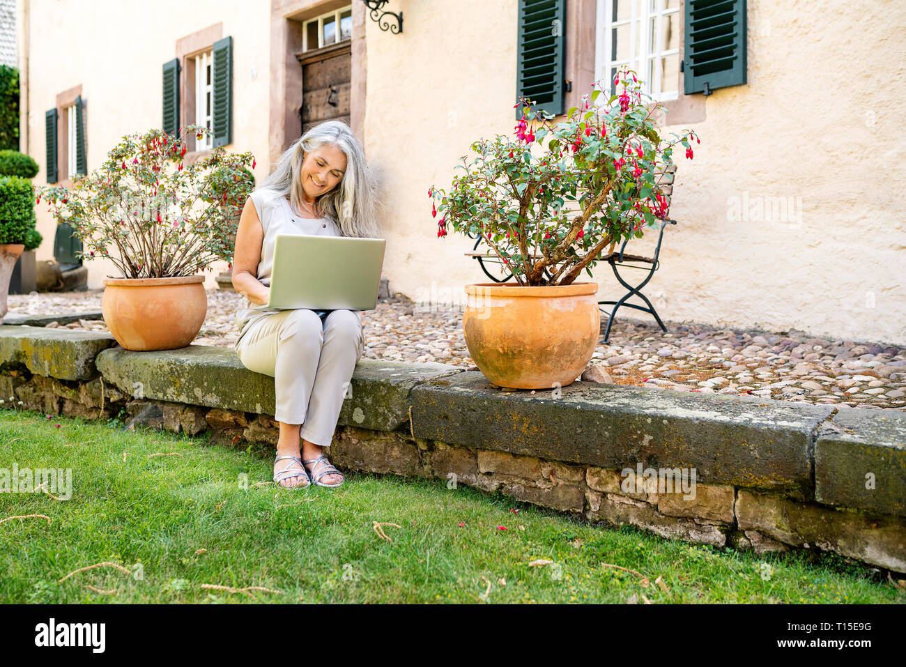 Femme aux longs cheveux gris assis sur la terrasse à country house en utilisant ordinateur portable Banque D'Images