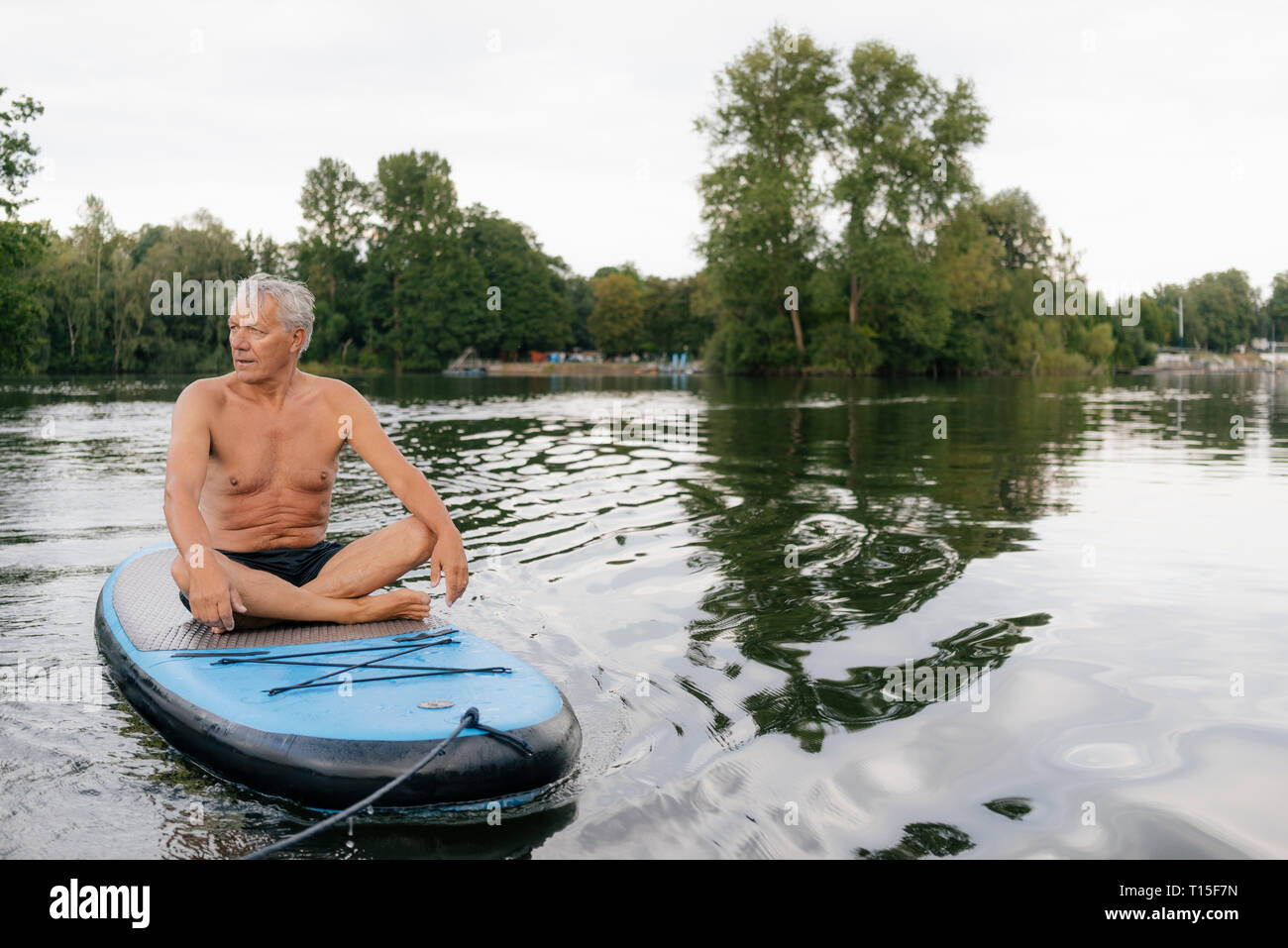 Senior man sitting on conseil SUP sur un lac Banque D'Images