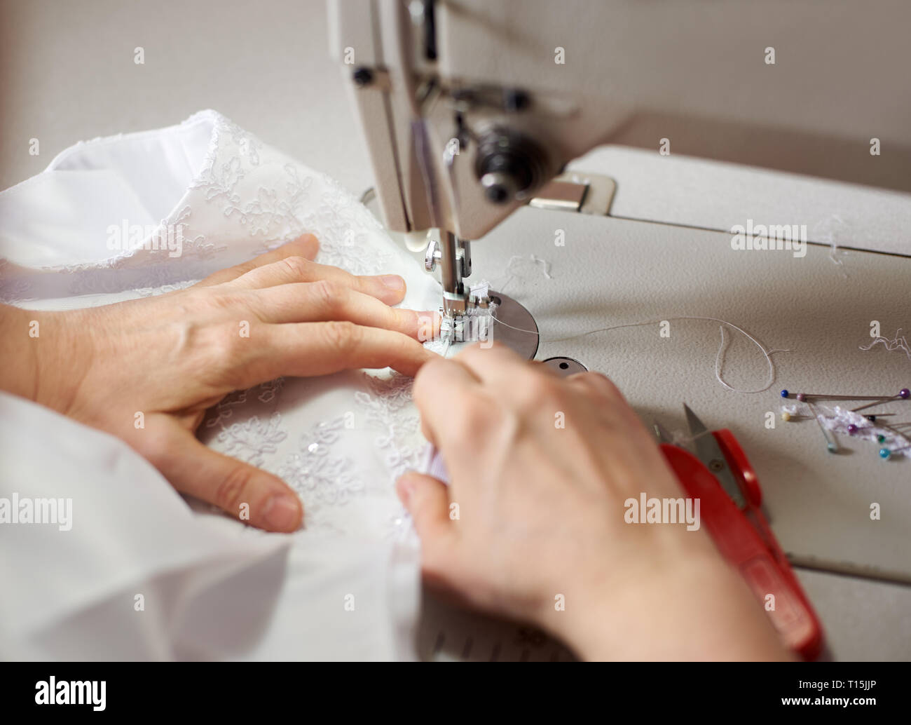 Les mains des femmes au lieu de travail de couture robe blanche avec les axes, les threads et ciseaux sur arrière-plan. Mettre couturière le tissu sous le pied-de-biche couture de Banque D'Images