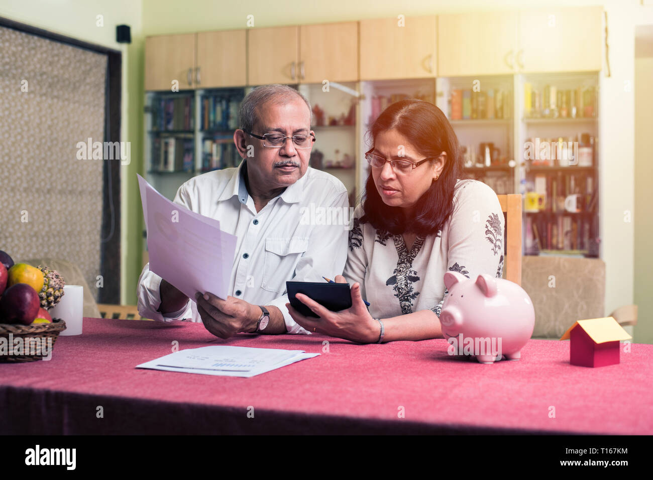 Un couple indien/asiatique senior qui effectue des opérations de financement à domicile et vérifie les factures avec un ordinateur portable, une calculatrice et de l'argent tout en étant assis sur un canapé à la maison Banque D'Images