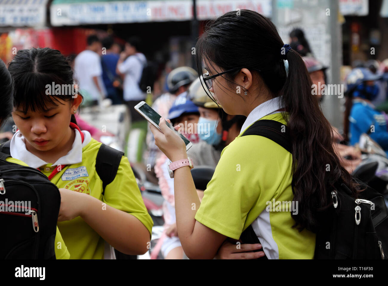 School girl stand avec i phone dans la main, l'accent sur smartphone après l'école, soirée close up tournage d'élève en t shirt uniforme, Vietnam Banque D'Images