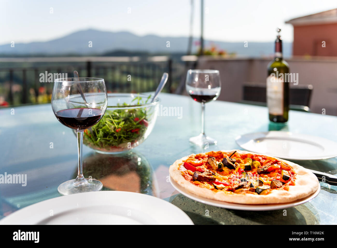 Pizza fraîche et salade sur table en verre à l'extérieur terrasse en Italie avec la sauce tomate légumes et deux verres de vin rouge bouteille Banque D'Images