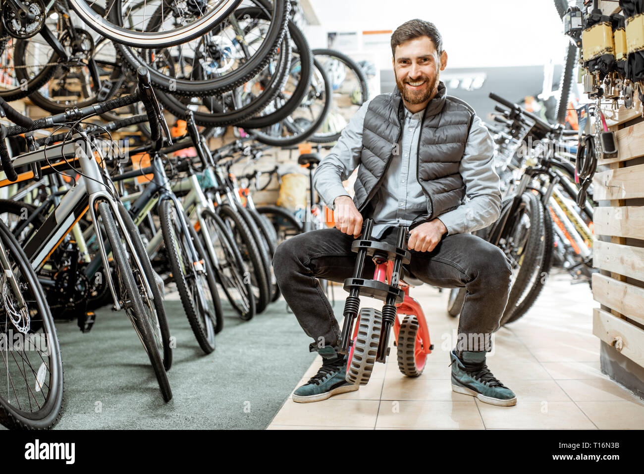 Portrait d'un homme drôle équitation children's location dans le magasin avec les vélos et les équipements sportifs Banque D'Images