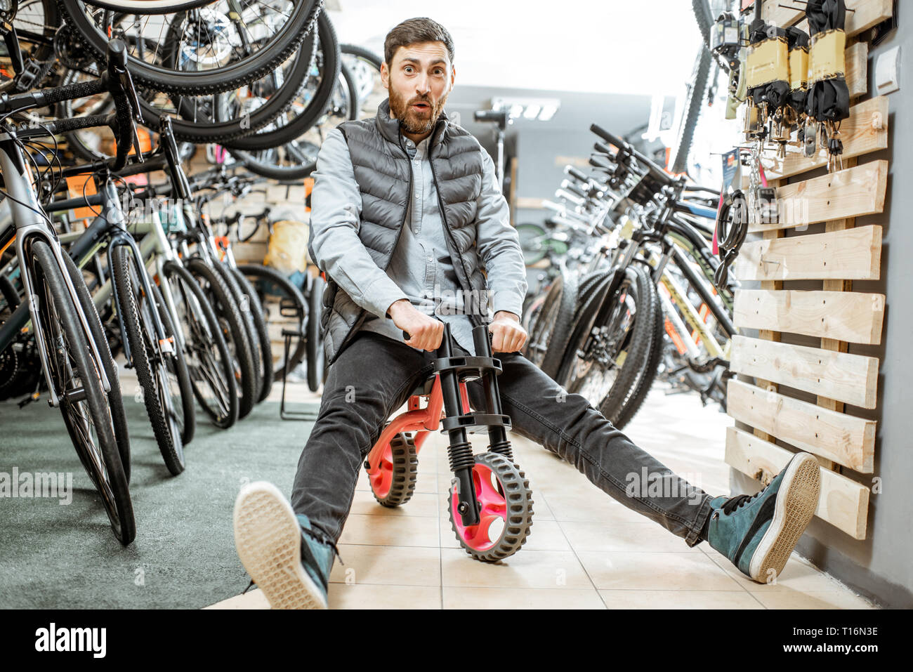 Portrait d'un homme drôle équitation children's location dans le magasin avec les vélos et les équipements sportifs Banque D'Images