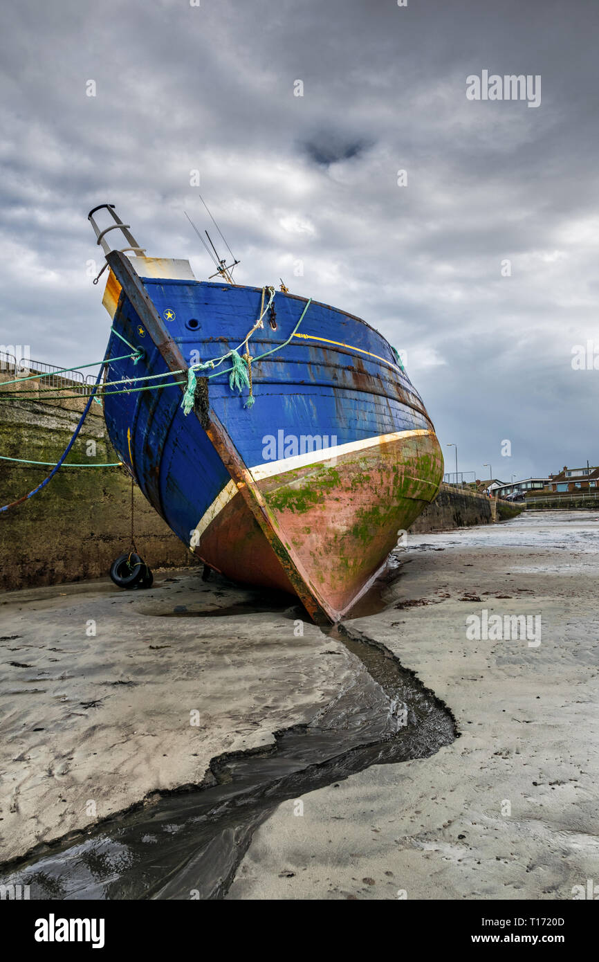 C'est un vieux bateau de pêche marée basse jusqu'à un quai à marée basse. Il est complètement hors de l'eau se penchant pour elle. Elle a été prise au point le plus de bavure Banque D'Images