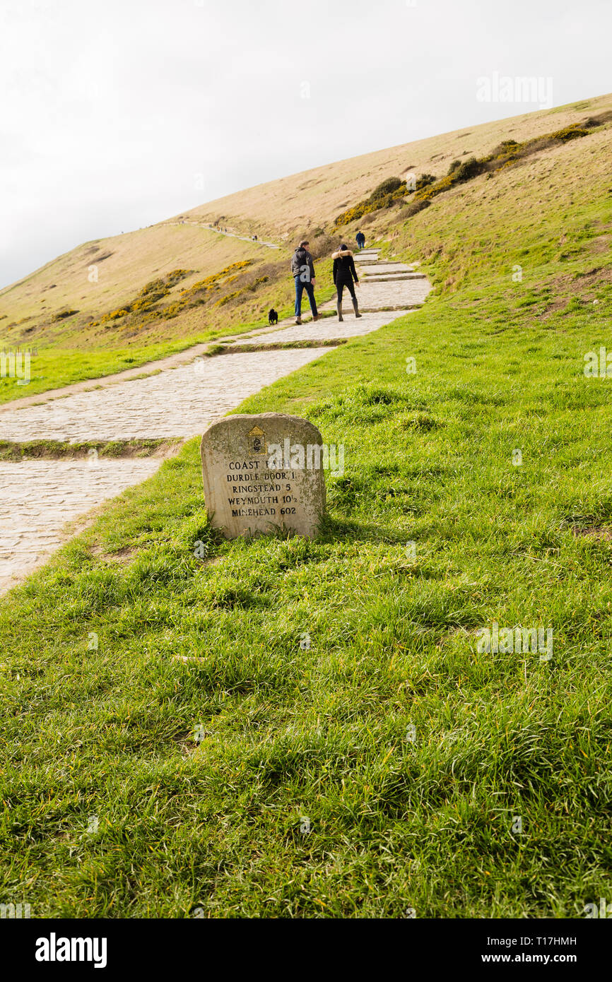 Sentier du littoral entre l'anse de Lulworth, et Durdle Dor montrant signe de pierre. Deux personnes sont vu marcher dans la distance. Banque D'Images