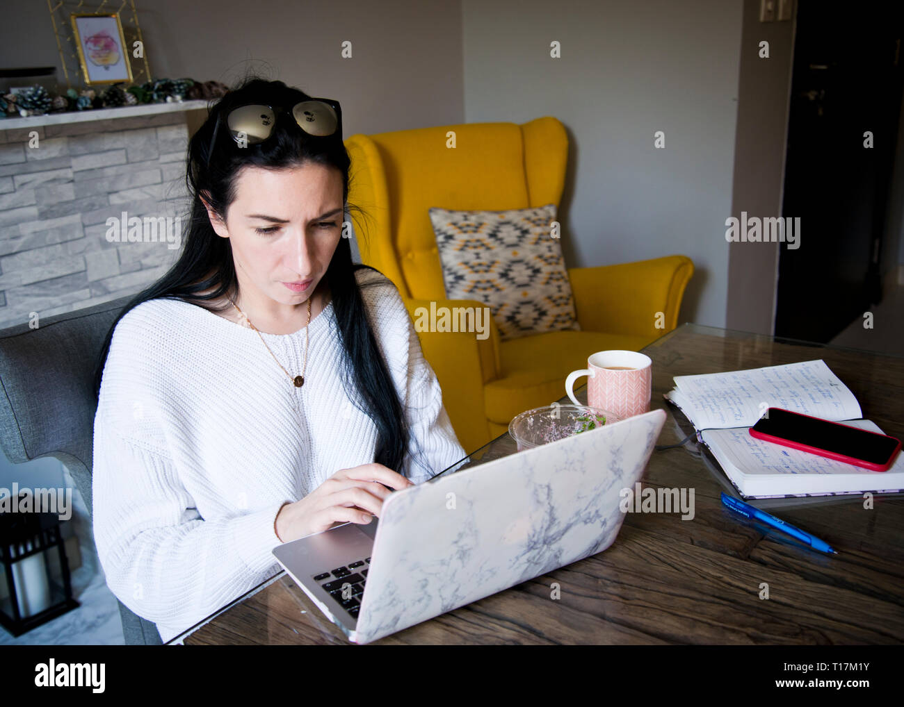 jeune femme travaillant assis à un bureau sur son ordinateur portable à la maison, stylo et papier à il prêt, tasse de thé pour se rafraîchir. Banque D'Images