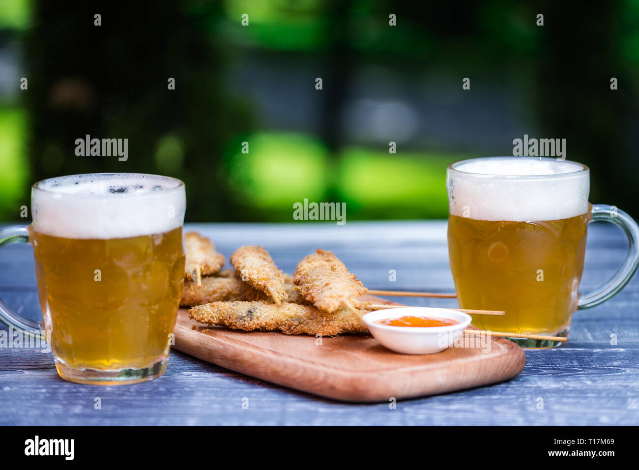 En-cas de la bière. Des ailes de poulet sur des bâtons et deux chopes de bière. Sur la planche à découper et vert fond d'été Banque D'Images