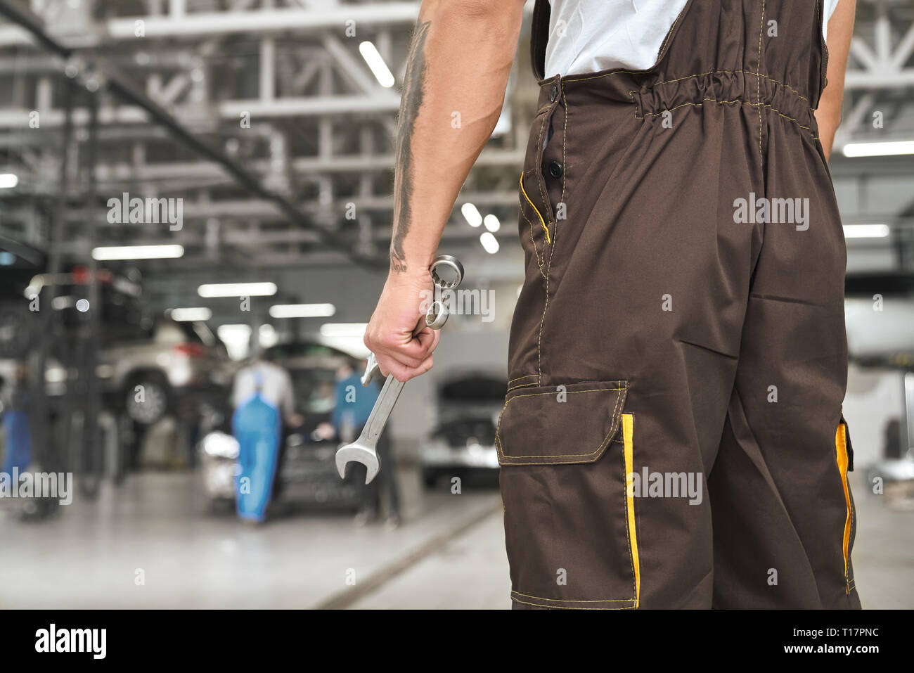 Vue arrière de mechanic standing in autoservice, outil clé de retenue, pour la fixation de l'automobile. En portant une combinaison marron réparateur, uniforme. Banque D'Images