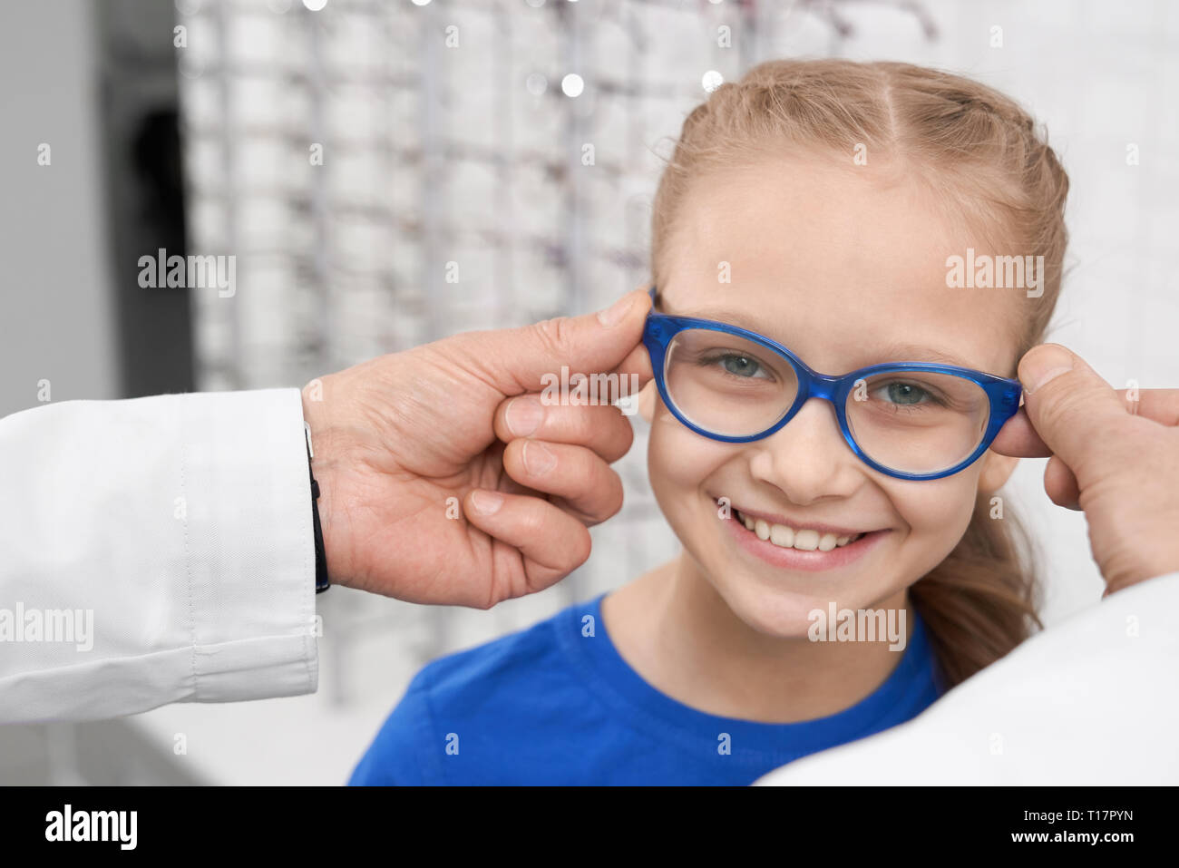 Close up de l'enfant en bleu les lunettes. Homme médecin ophtalmologiste aider jolie fille de choisir des lunettes. Le médecin et le patient en ophtalmologie clinique. Concept de soins de santé. Banque D'Images