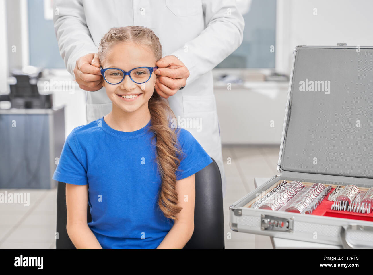 Médecin ophtalmologiste en blouse blanche portant des lunettes bleu sur patient. Pretty smiling girl sitting and looking at camera. Concept de traitement et de correction de la vue. Banque D'Images