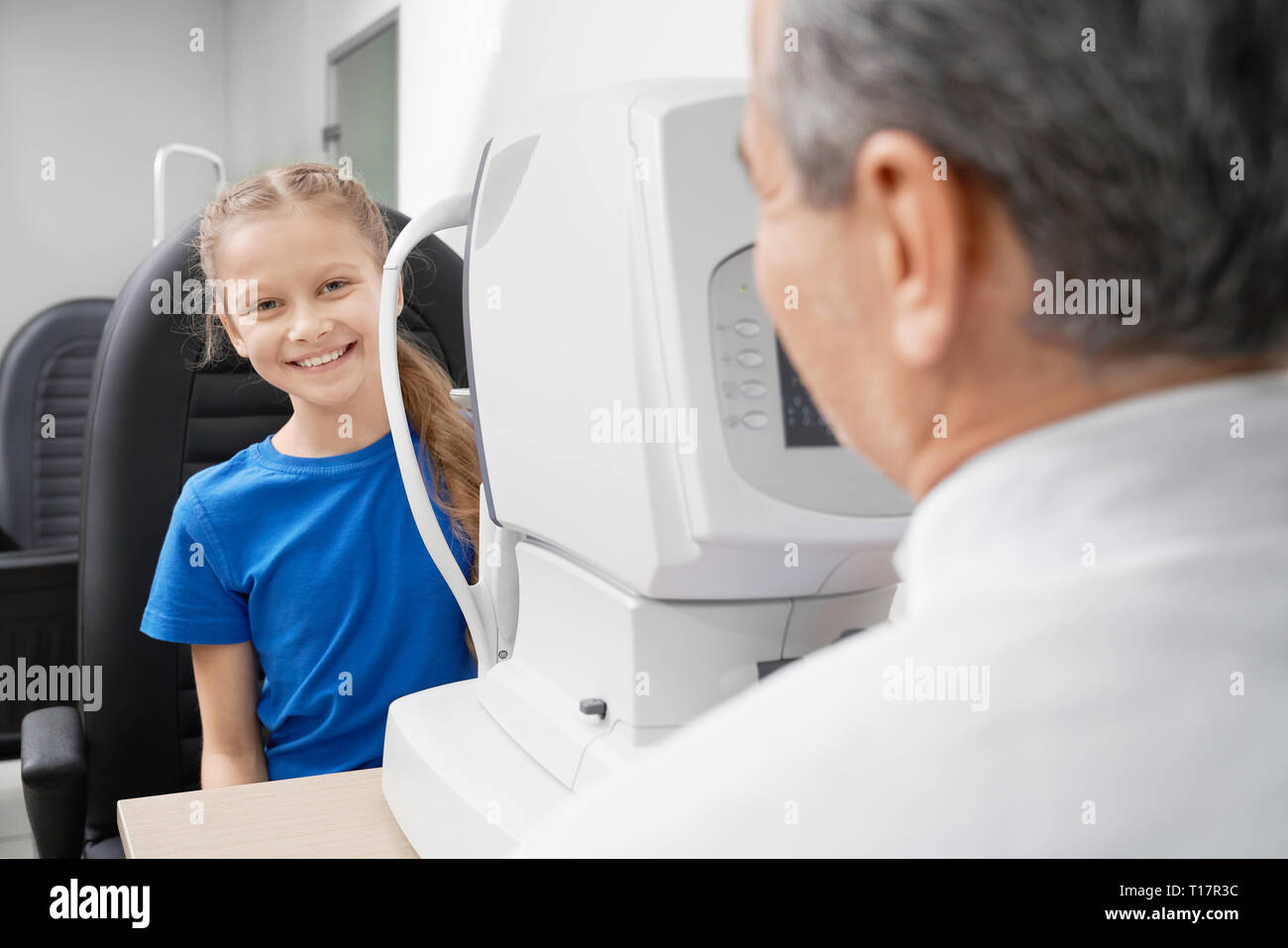 Jeune, jolie vue dans l'essai patient opticien moderne office de clinique médicale. Smiling girl sitting at table avec équipement d'optométrie. Low angle vision avec eye machine de test. Banque D'Images