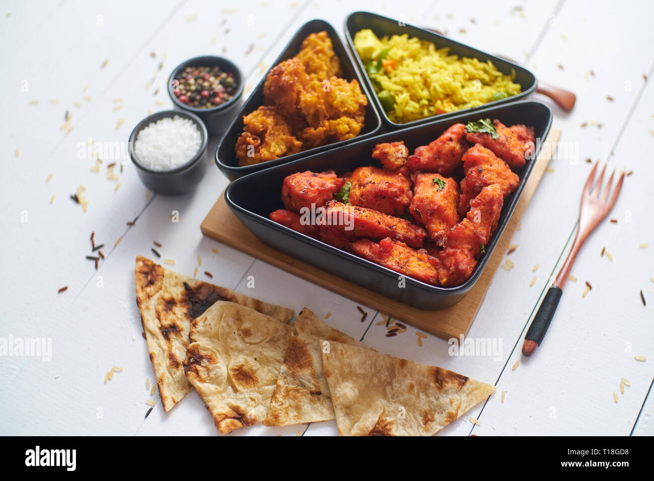 Poulet frit indien épicé servi avec du riz aux légumes au curry, oignons bhajia, pain naan. Placé sur une table en bois blanc. Banque D'Images