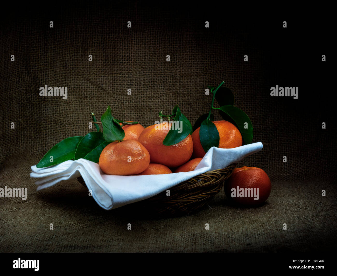 Les oranges avec des feuilles dans le panier, sombre de style ciaroscuro still life. Sur fruits hessian . Banque D'Images