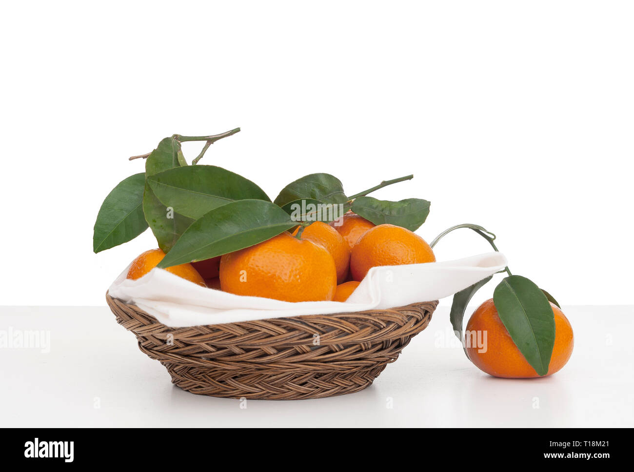 Mandarines, oranges juteuses petites avec des feuilles dans panier en osier avec serviette, serviette. Des fruits sur fond blanc, isolé contre. Banque D'Images