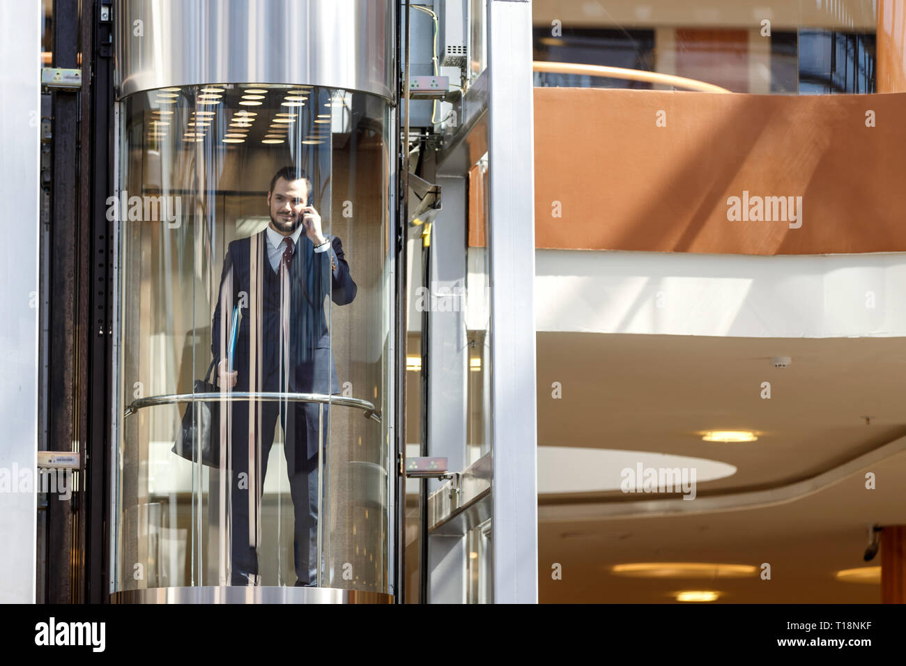 Businessman dans l'ascenseur en verre moderne de parler par le téléphone et holding briefcase Banque D'Images