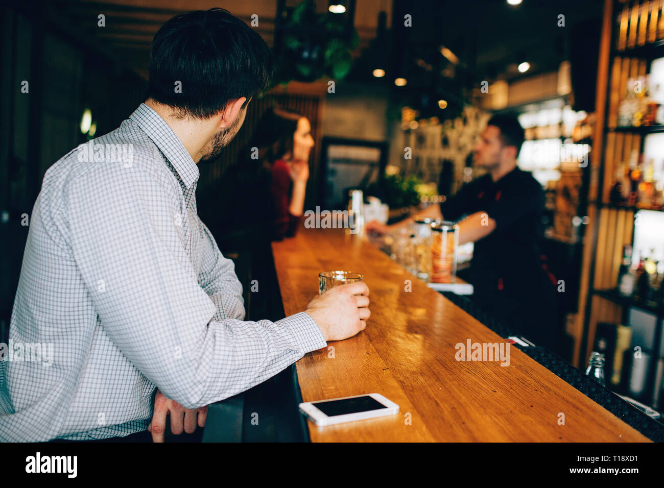 Bien construit et beau mec est assis au stand du barman et de boire de l'alcool. Son téléphone est en dehors de lui. Guy est à la recherche du côté où Banque D'Images