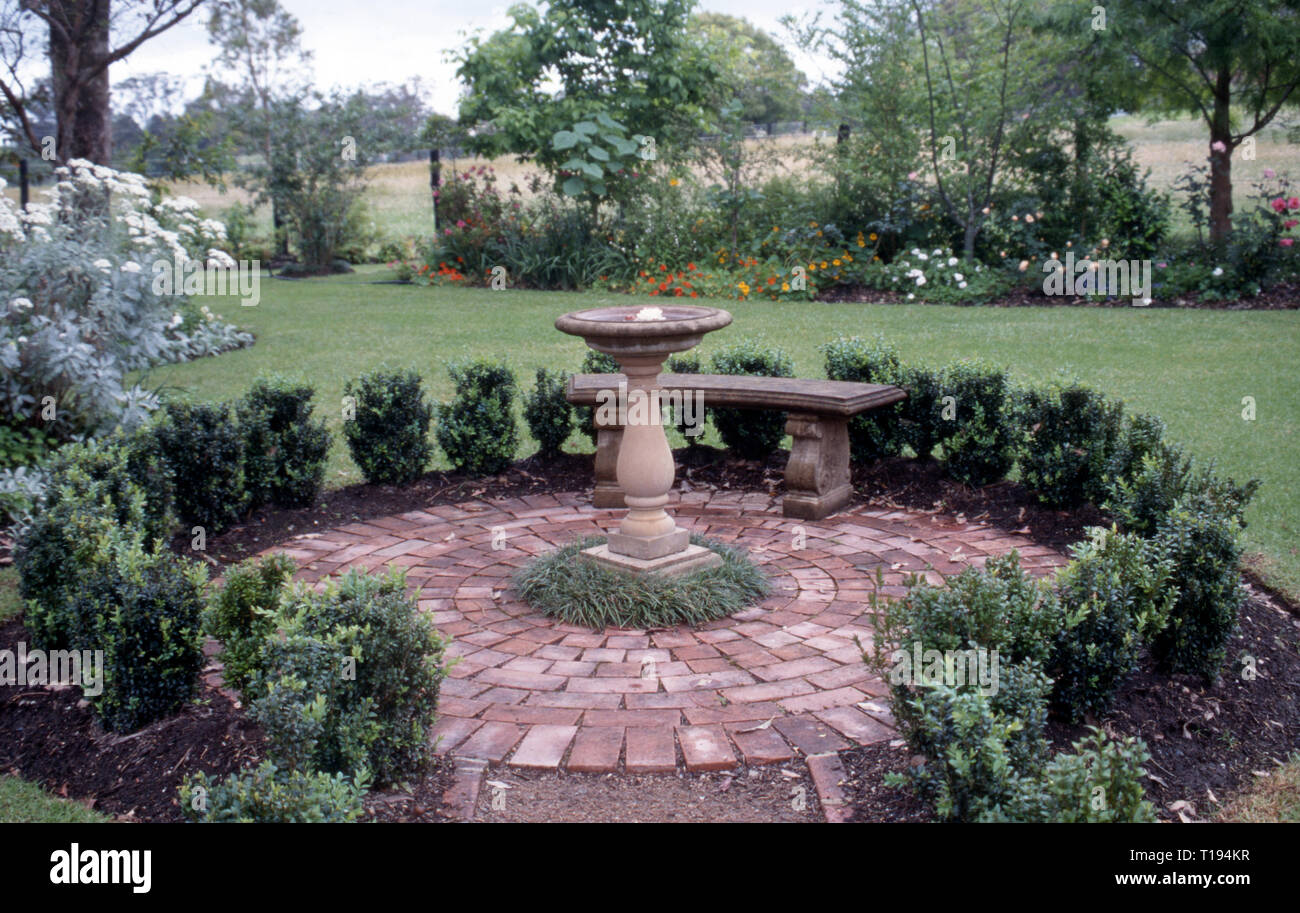 Jardin brique circulaire bordé de petites haies, BAIN D'OISEAUX CENTRE MONDO AVEC DE PLUS EN PLUS D'HERBE AUTOUR DE LA BASE. NEW SOUTH WALES, AUSTRALIE Banque D'Images