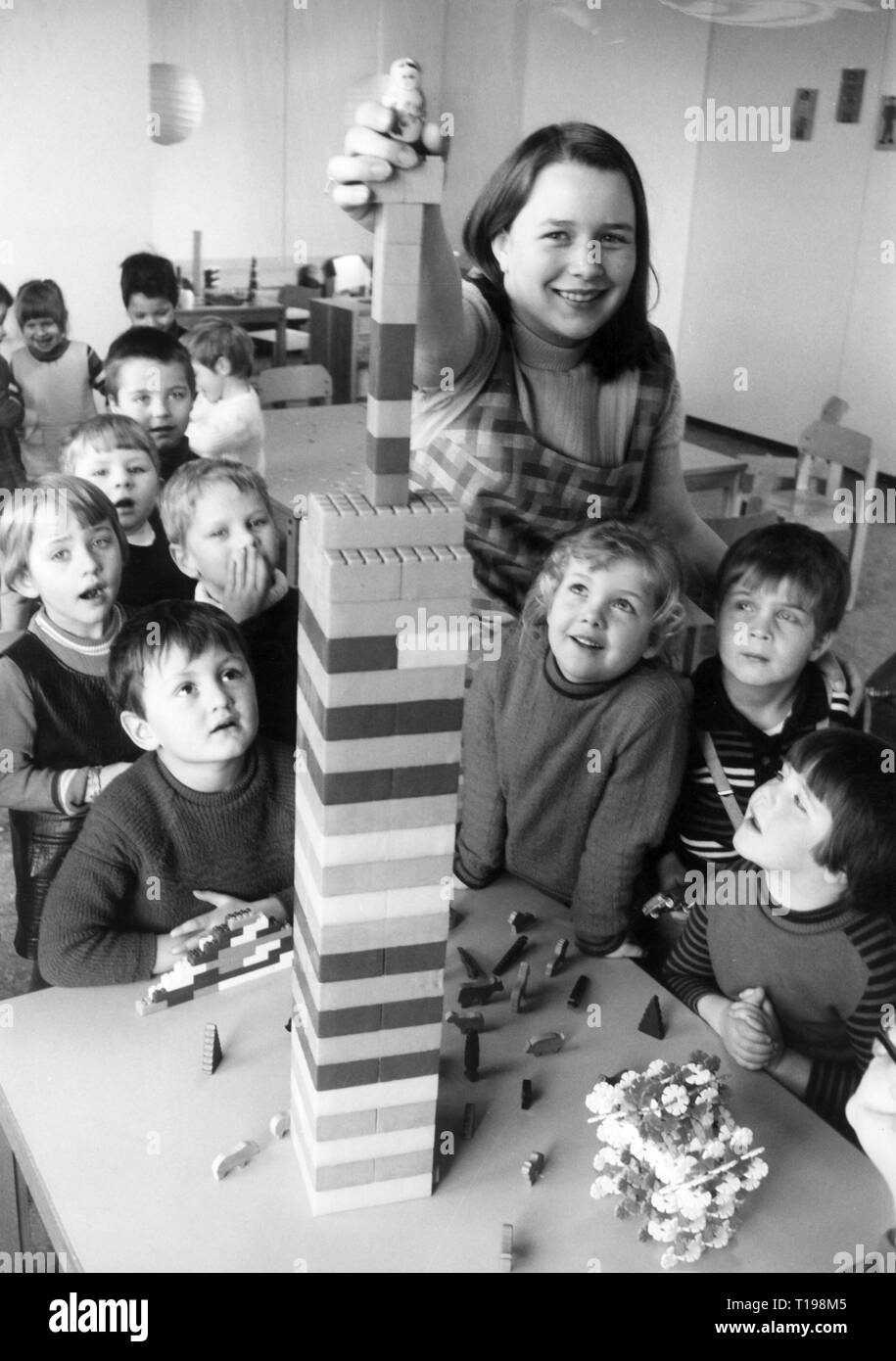 Les gens, les enfants, la maternelle / lit bébé / école approuvée, enseignant de maternelle mettre poupée sur tower fait de jouets de construction, des années 1970, à Additional-Rights Clearance-Info-Not-Available Banque D'Images