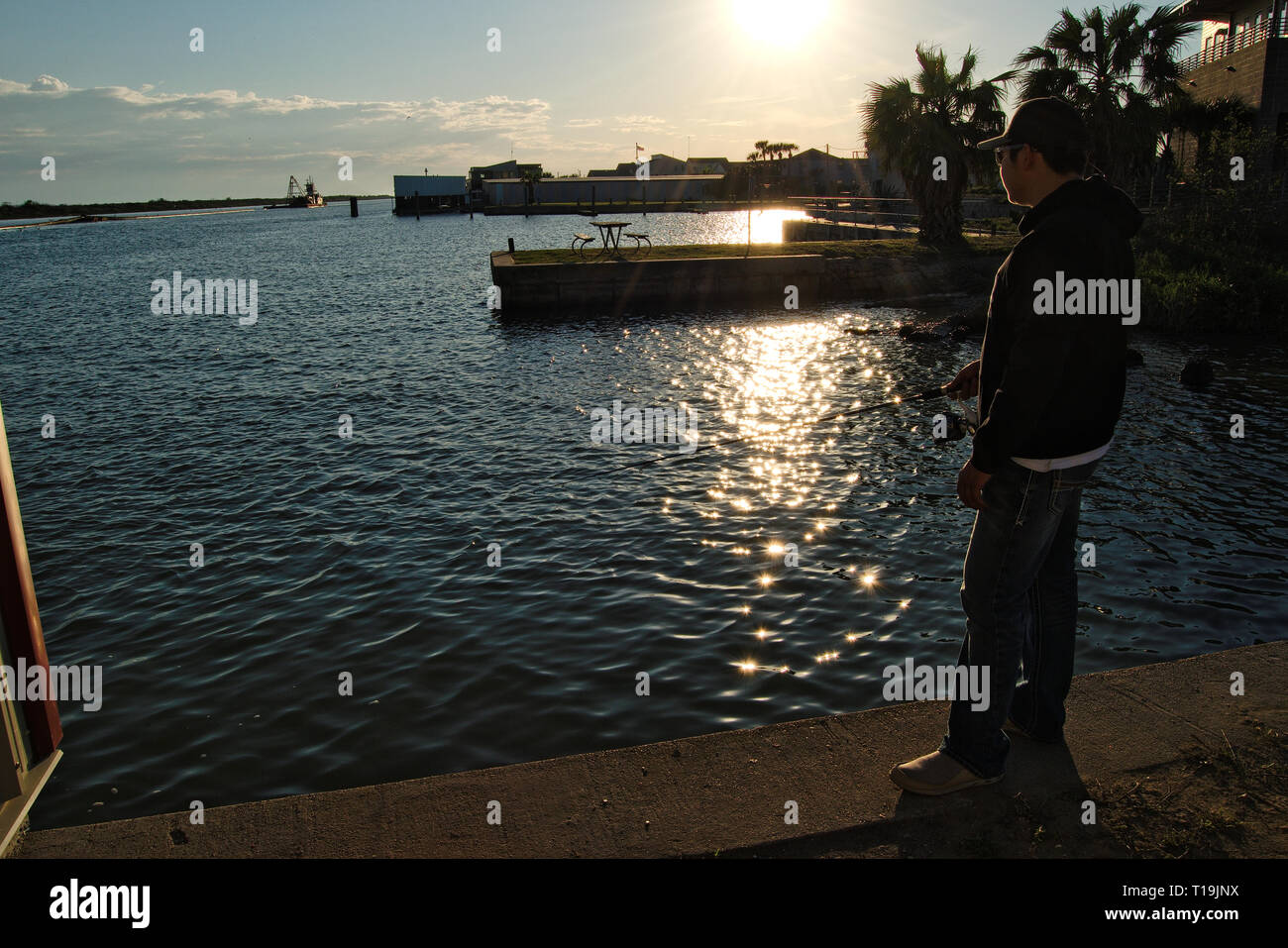 Jeune homme pêche sur un quai de ciment au coucher du soleil Banque D'Images