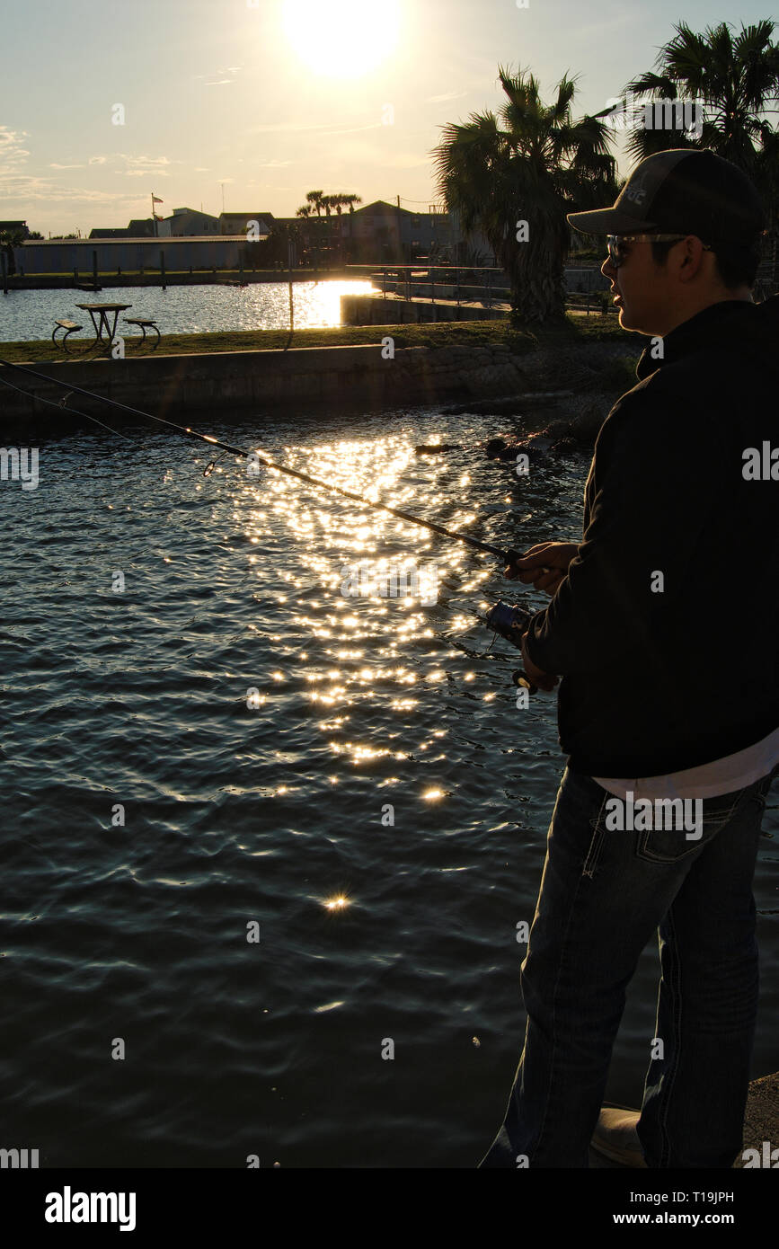 Jeune homme pêche sur un quai de ciment au coucher du soleil Banque D'Images