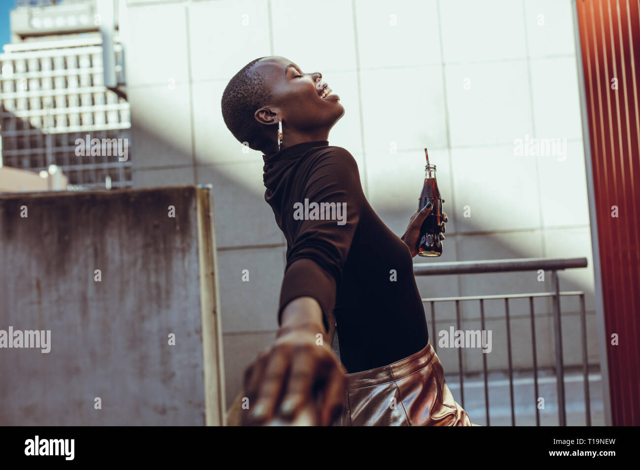 Vue latérale d'African Woman leaning d'une balustrade avec bouteille de boisson. Woman sur sa fin de semaine. Banque D'Images