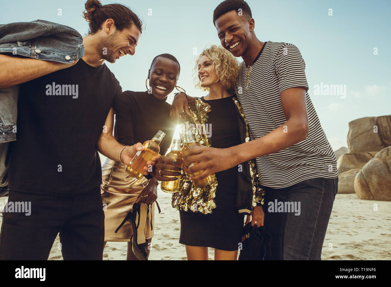 Groupe multi-ethnique des amis à la plage d'avoir des bières. Les jeunes hommes et femmes à la plage de fonctionnement des bières. Banque D'Images