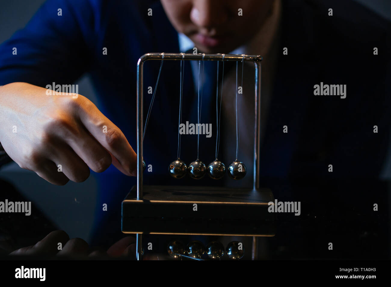 Méconnaissable businessman pulling petite bille de métal de Newton cradle et en observant l'élan au cours de table en verre Banque D'Images